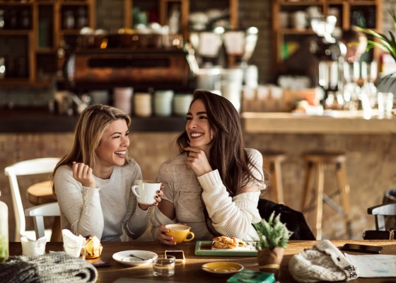 Young happy women talking and laughing while drinking coffee together in coffee shop.