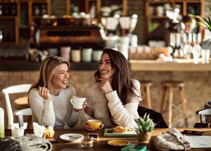 Young happy women talking and laughing while drinking coffee together in coffee shop.