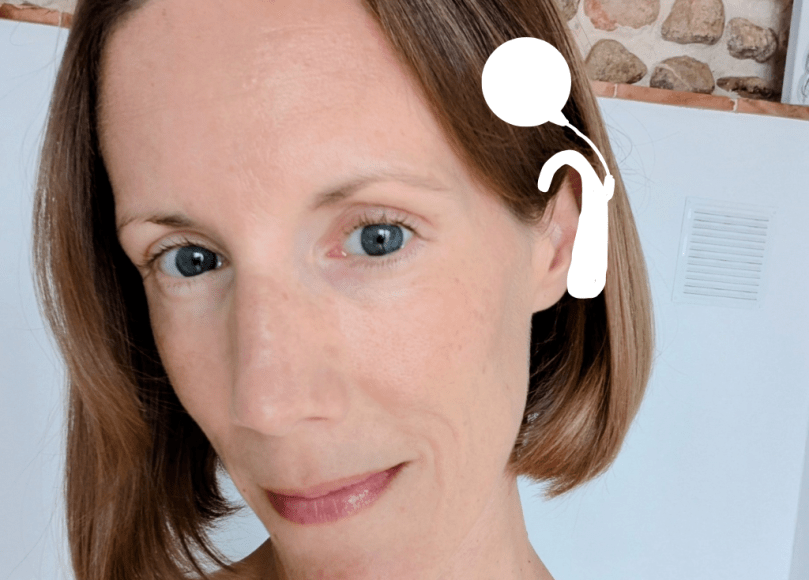 Headshot of Carly - woman in her early 40s with brown hair in a bob style, wearing a yellow top. Over the photo is a drawn-on white cochlear implant over her left ear.