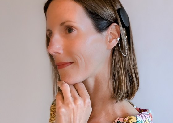 Photo of Carly's head and shoulders. She is looking reflective, with her hand under her chin, proudly showing off her CI processor and safety chain accessory.